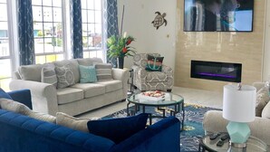 Una sala de estar con un sofá azul, dos sillones, una mesa de centro y un televisor montado en la pared.