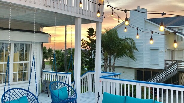 Una terraza techada al aire libre con asientos azules, luces colgantes y vistas al atardecer.