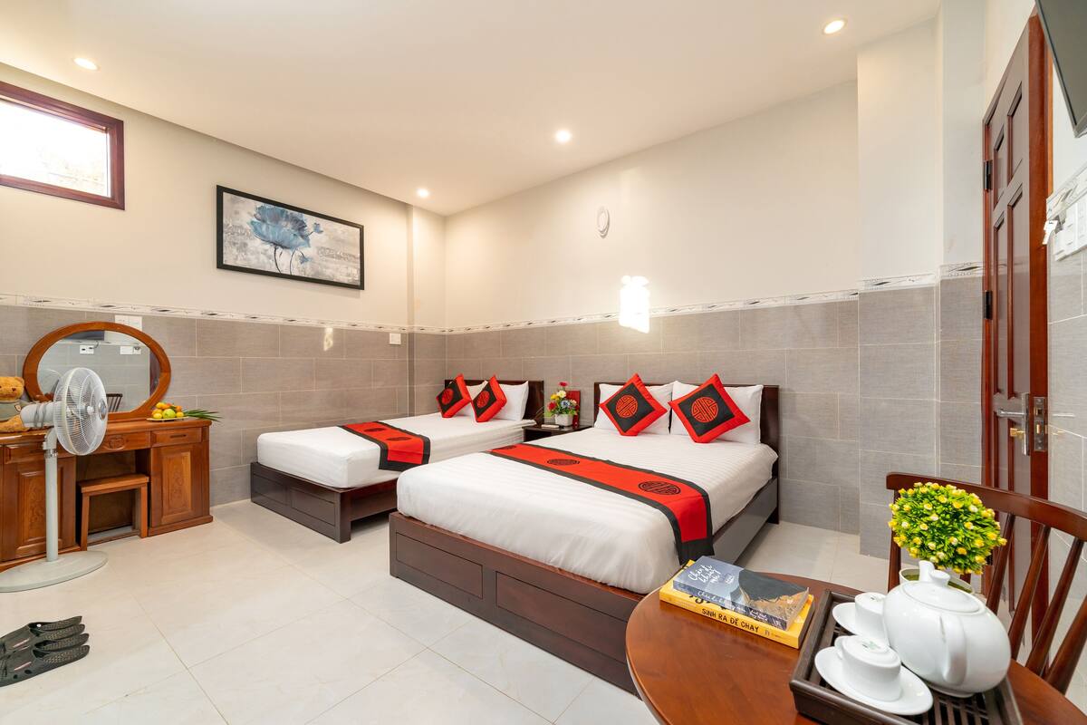 A hotel room with two beds, a wooden desk with a fan, a mirror, and a small table with a teapot and cups.