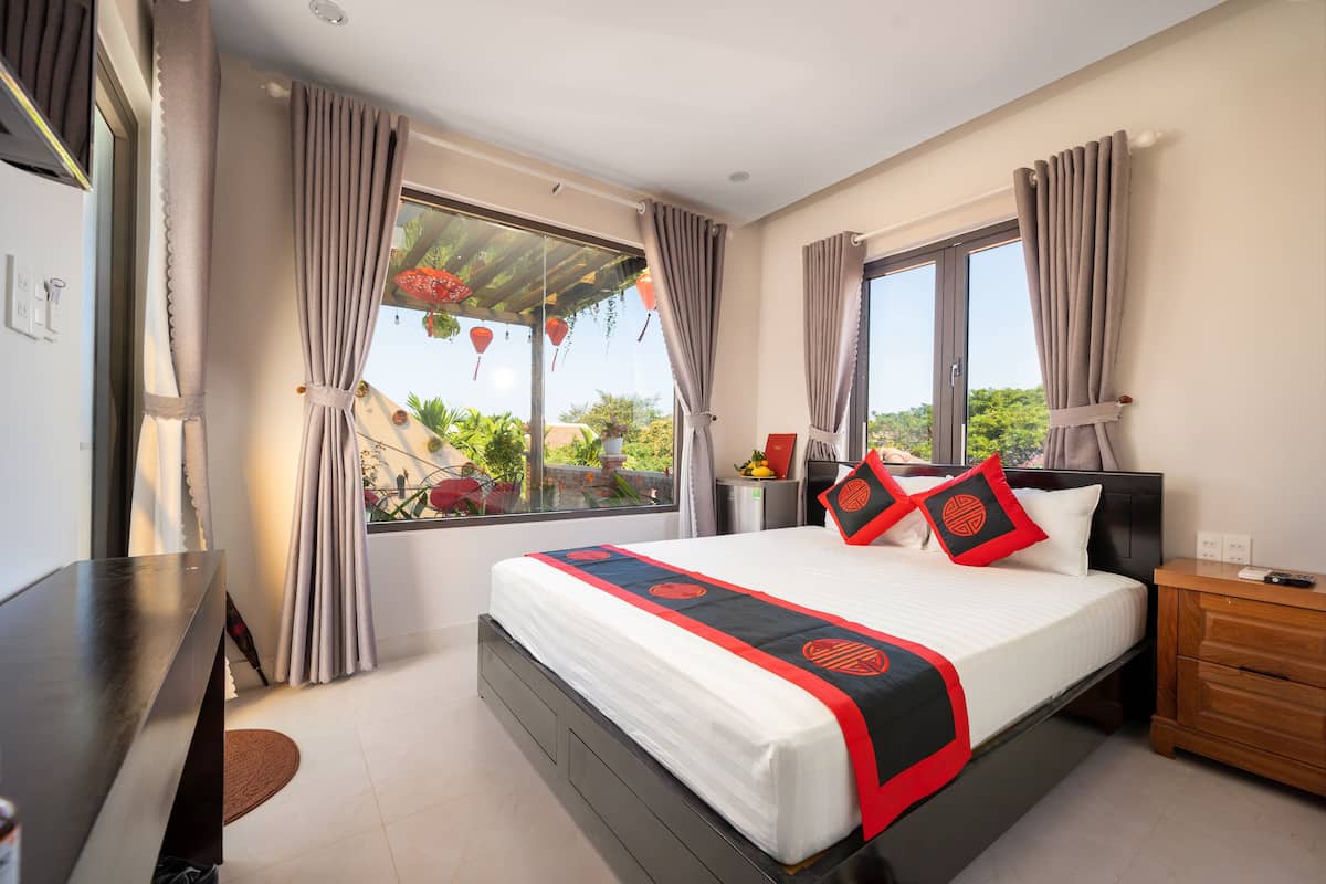 A bedroom with a large bed, a wooden nightstand, a desk, and a window with curtains.