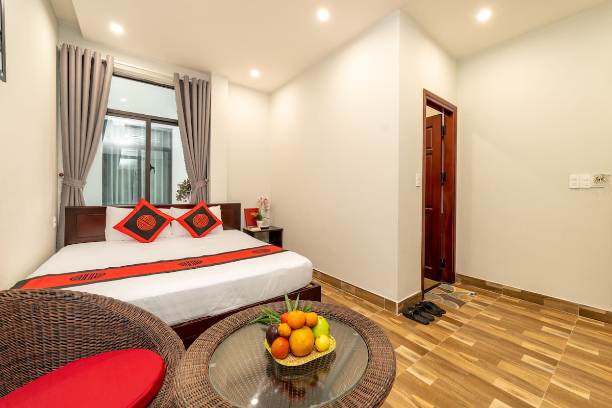 A hotel room with a bed, a round table with fruit, a wicker chair, and a wooden floor.