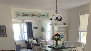Ruokailutilassa on puinen pöytä ja valkoiset tuolit, kattokruunu sekä seinällä kyltti, jossa lukee: ”Hart’s River House”.