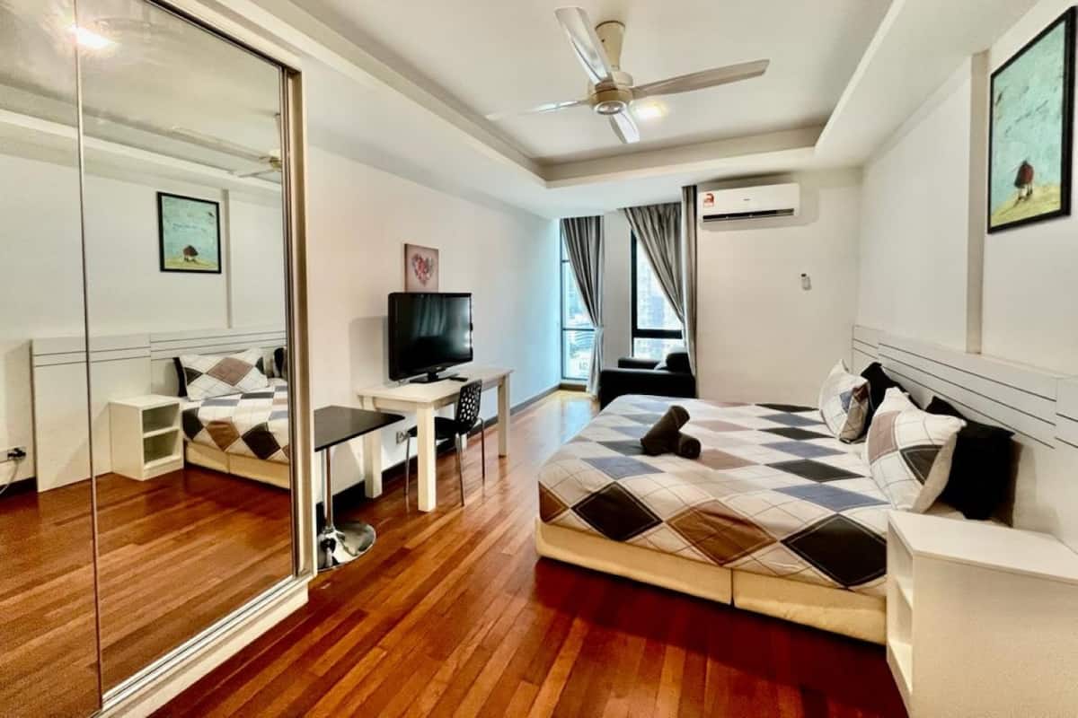 Una habitación de hotel moderna con una cama grande, un escritorio con televisor, un ventilador de techo y un espejo amplio.