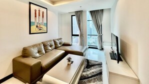 Un salon moderne avec un canapé, une table basse et un téléviseur. Il y a un tableau au mur et une fenêtre avec des rideaux.