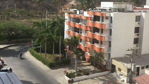 Un edificio de varios pisos con balcones, una calle pavimentada y palmeras.