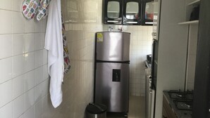 Una cocina compacta con paredes de azulejos blancos, un refrigerador de acero inoxidable, un lavamanos y una estufa.