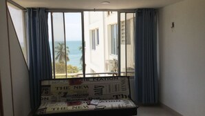 Una habitación con una cama cubierta de periódicos, ventanas amplias con cortinas y vista al océano y palmeras.
