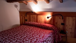 Une pièce aux murs lambrés, avec un lit, une lampe fixée au mur et une poutre en bois au plafond.