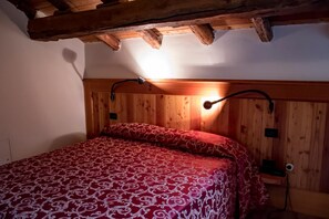 A wooden-paneled room with a bed, a wall-mounted lamp, and a wooden ceiling beam. - Villa Della Regina (Gressoney-la-Trinite)