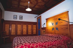 A bedroom with a wooden wardrobe, a bed with a patterned bedspread, and a ceiling with exposed beams. - Villa Della Regina (Gressoney-la-Trinite)