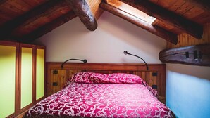 Une chambre avec un plafond en pente, des poutres en bois, un lit recouvert d’une couvre-lit à motifs et une tête de lit en bois.