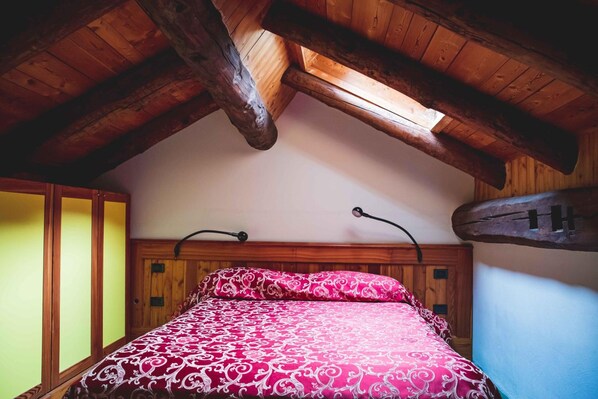 A bedroom with a sloped ceiling, wooden beams, a bed with a patterned bedspread, and a wooden headboard.