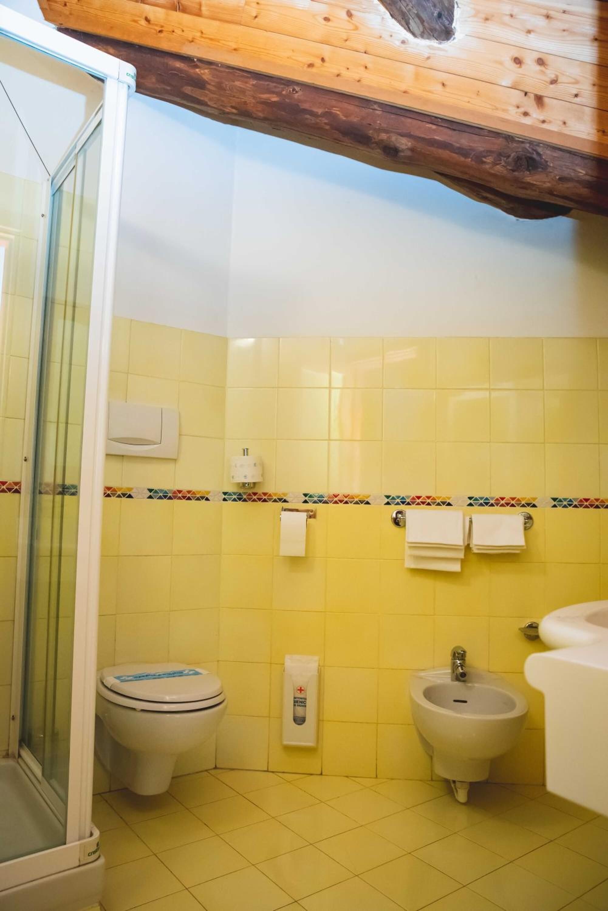 Une salle de bain avec des carreaux jaunes, une douche en verre, des toilettes, un bidet et un porte-serviettes.