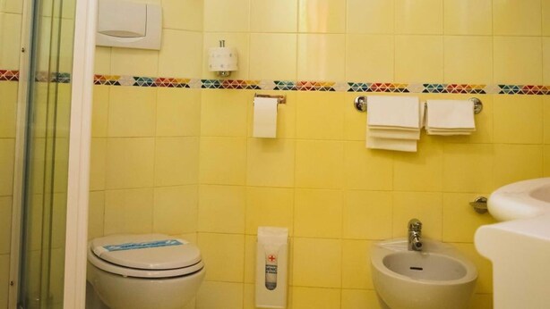 Une salle de bain avec des carreaux jaunes, une douche en verre, des toilettes, un bidet et un porte-serviettes.