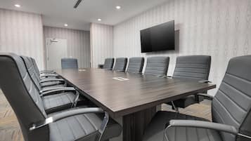 A conference room with a long table, six chairs, a flat-screen TV, and patterned wallpaper.
