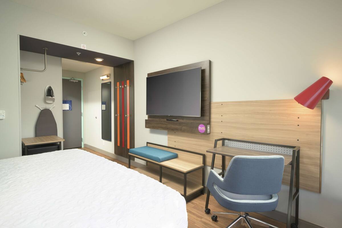 A hotel room with a large bed, a desk, a chair, a TV, and a red lamp.