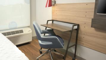 Un dormitorio con cama, escritorio con silla, televisión instalada en la pared y una lámpara roja.
