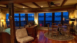 Um quarto acolhedor com piso de madeira, uma cadeira estampada em zebra, uma mesa de jantar com cadeiras e grandes janelas com vista para a água.