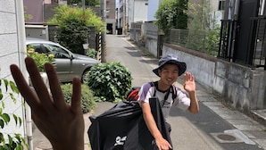 A narrow residential street with houses on both sides, a parked car, and a person with a backpack. - Hostel KIKO (Sendai)