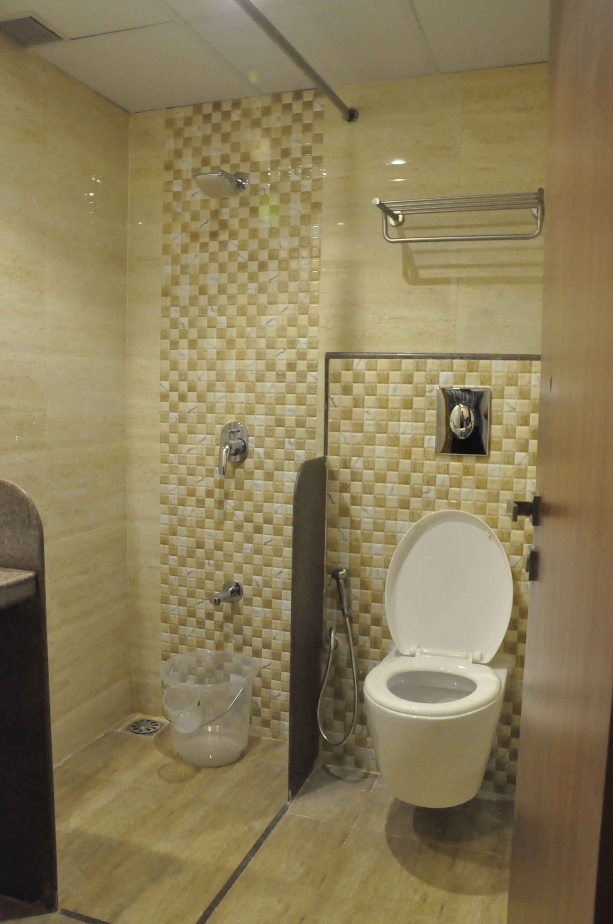 A bathroom with a tiled shower wall, a toilet, and a hand dryer.