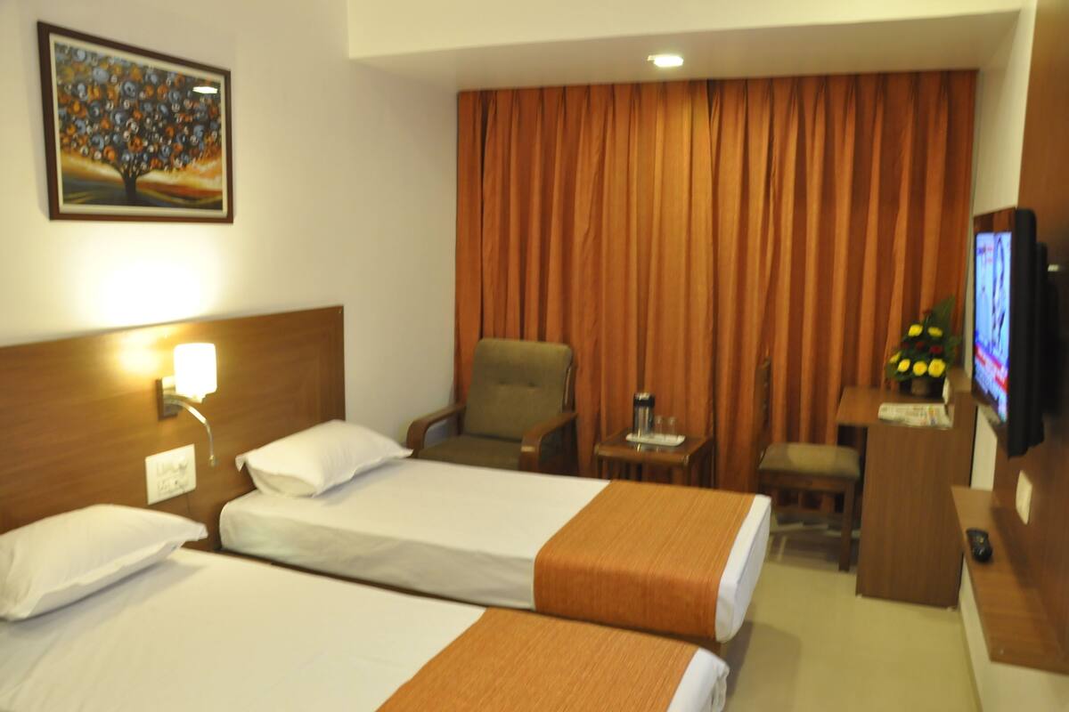 Habitación de hotel con dos camas, un escritorio con silla, una televisión y un cuadro en la pared.