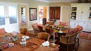 A dining area with a wooden table set for four, surrounded by wicker chairs with patterned cushions. - Branley Lodge (Hillcrest)