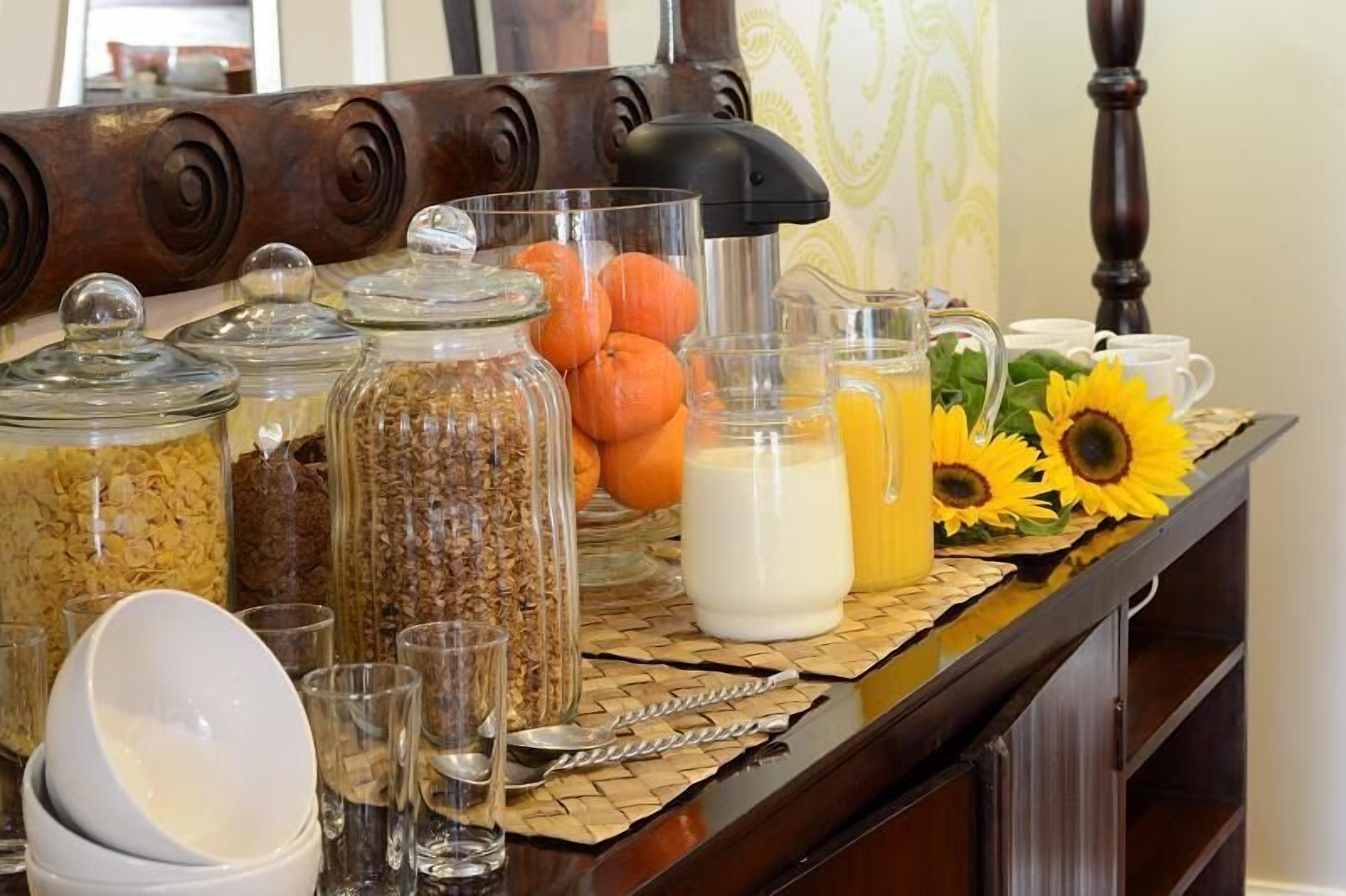 Un bufé de desayuno con diversos alimentos y bebidas, incluyendo botes de granola, calabazas y una jarra de jugo de naranja.