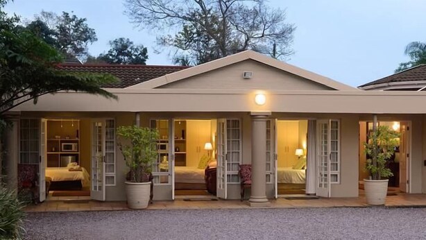 A hotel with a beige exterior, large glass doors leading to a room with a bed and a lamp. - Branley Lodge (Hillcrest)