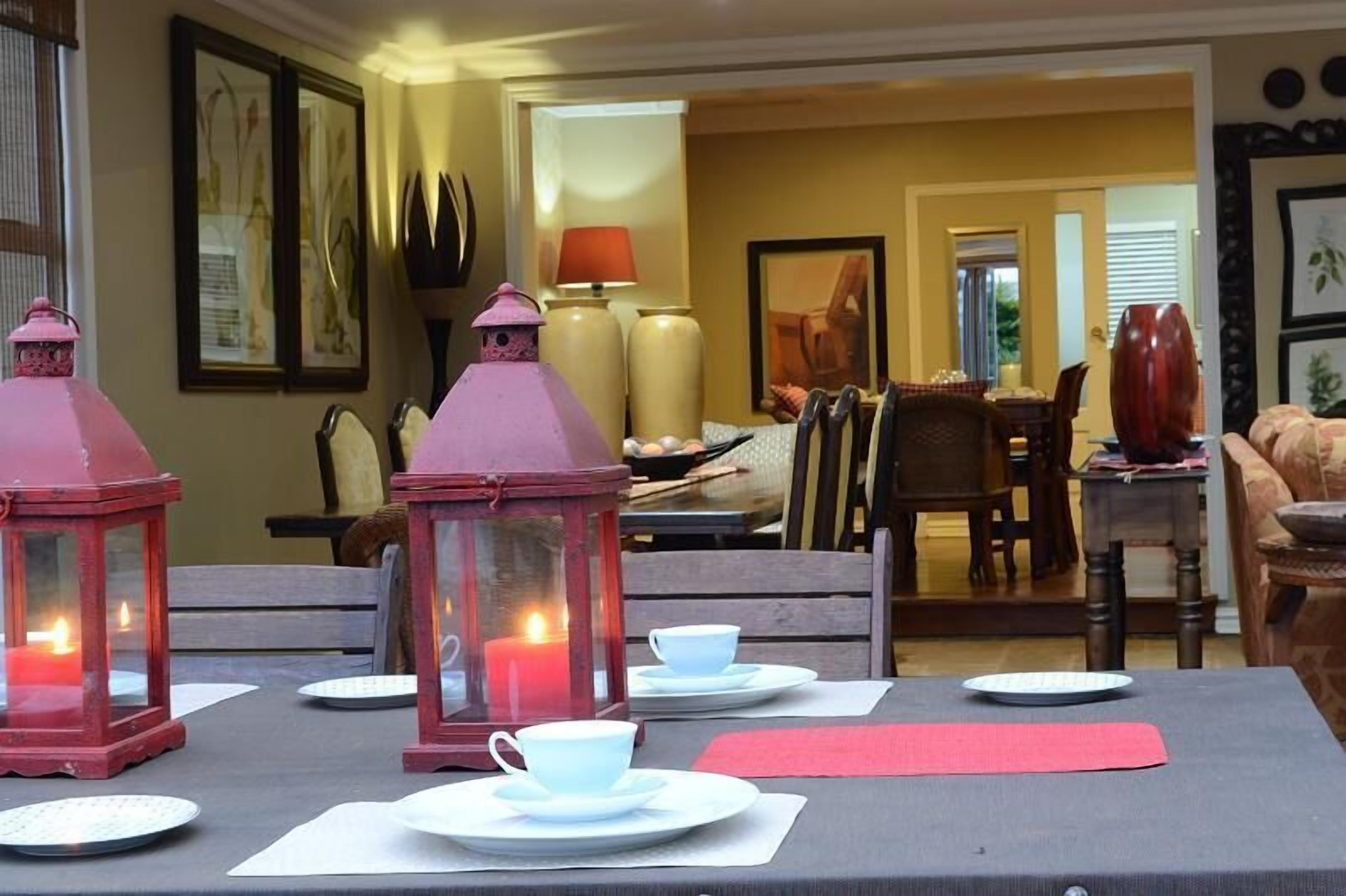 Comedor con una mesa preparada para dos personas, con faroles rojos, platos blancos y tazas.