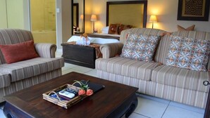A hotel room with a bed, two striped sofas, a coffee table with books and flowers, and a mirror on the wall. - Branley Lodge (Hillcrest)