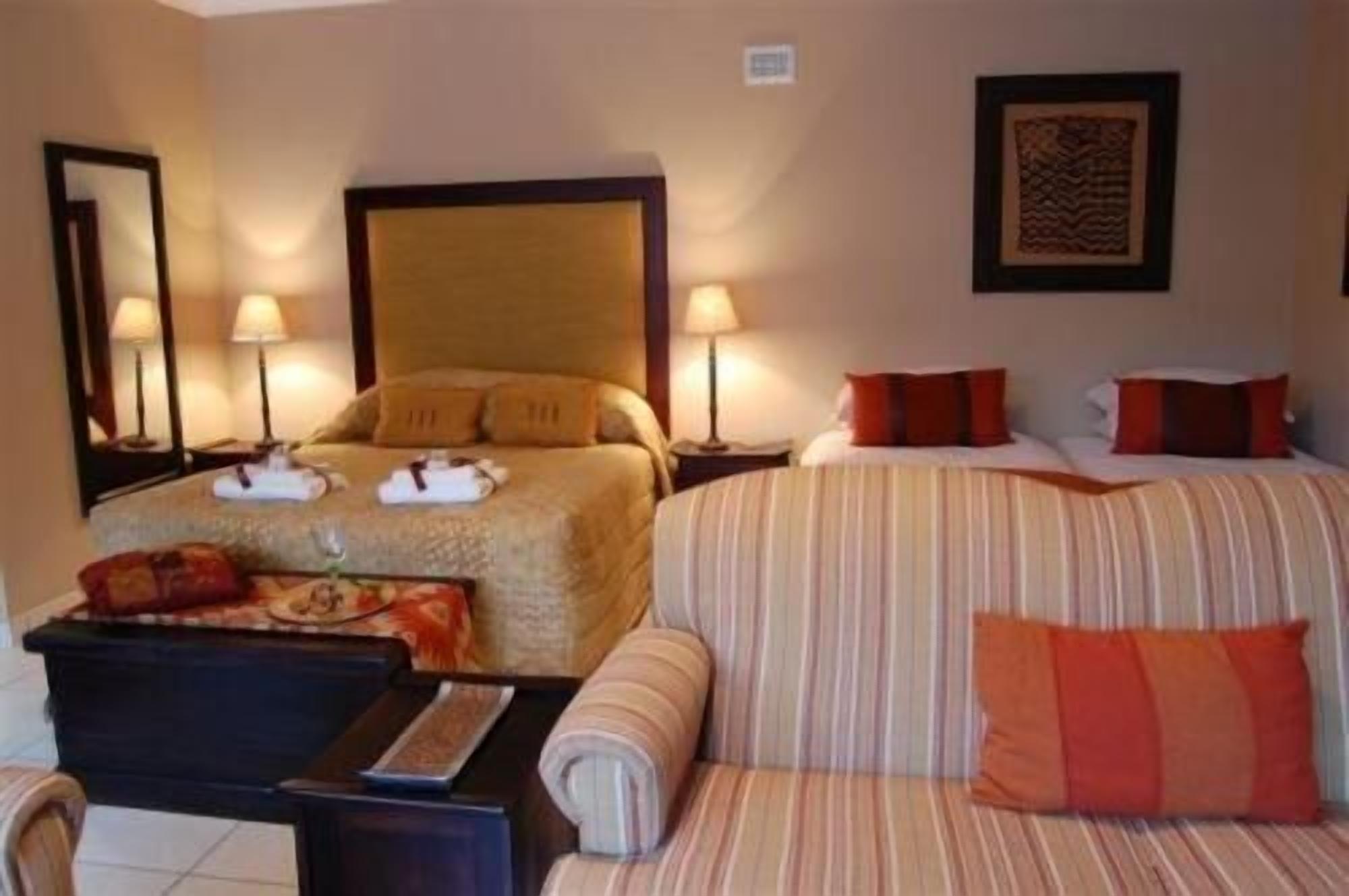 A hotel room with two beds, a sofa, a desk, and two lamps.