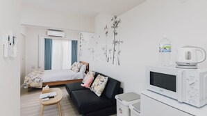A modern hotel room with a bed, a sofa, a microwave, and a water bottle. - AFP Tennoji Apartment (Osaka)