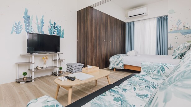 A modern hotel room with a flat-screen TV, wooden furniture, a bed with a tropical print, and a large window with curtains. - AFP Tennoji Apartment (Osaka)