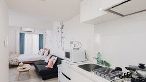A compact living space with a kitchenette, a bed with blue curtains, a microwave, a small refrigerator, and a sink. - AFP Tennoji Apartment (Osaka)