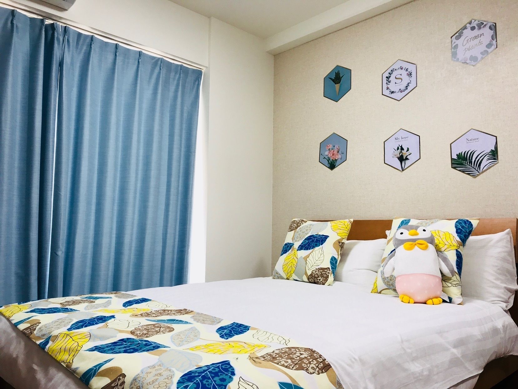 A bedroom with a bed, blue curtains, and wall decorations including hexagonal frames with floral and nature-themed designs.
