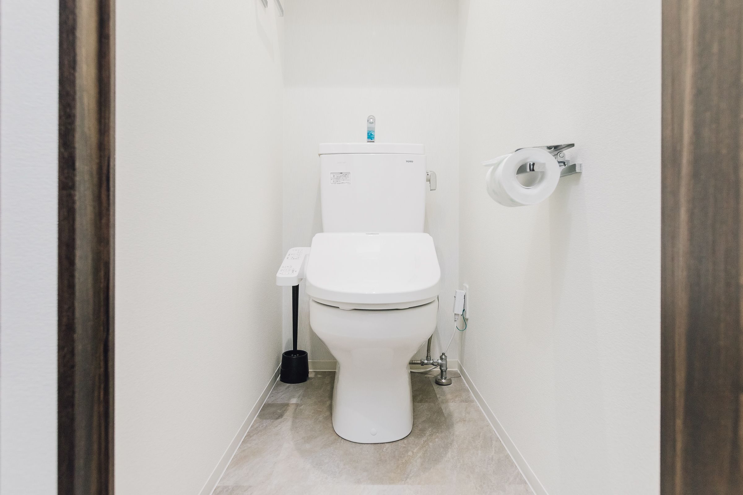A small, clean bathroom with a white toilet, a toilet paper holder, and a black cleaning brush.