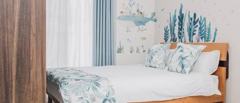 A bedroom with a wooden bed, white bedding, a tropical leaf-patterned throw, and a wall mural of underwater scenery.