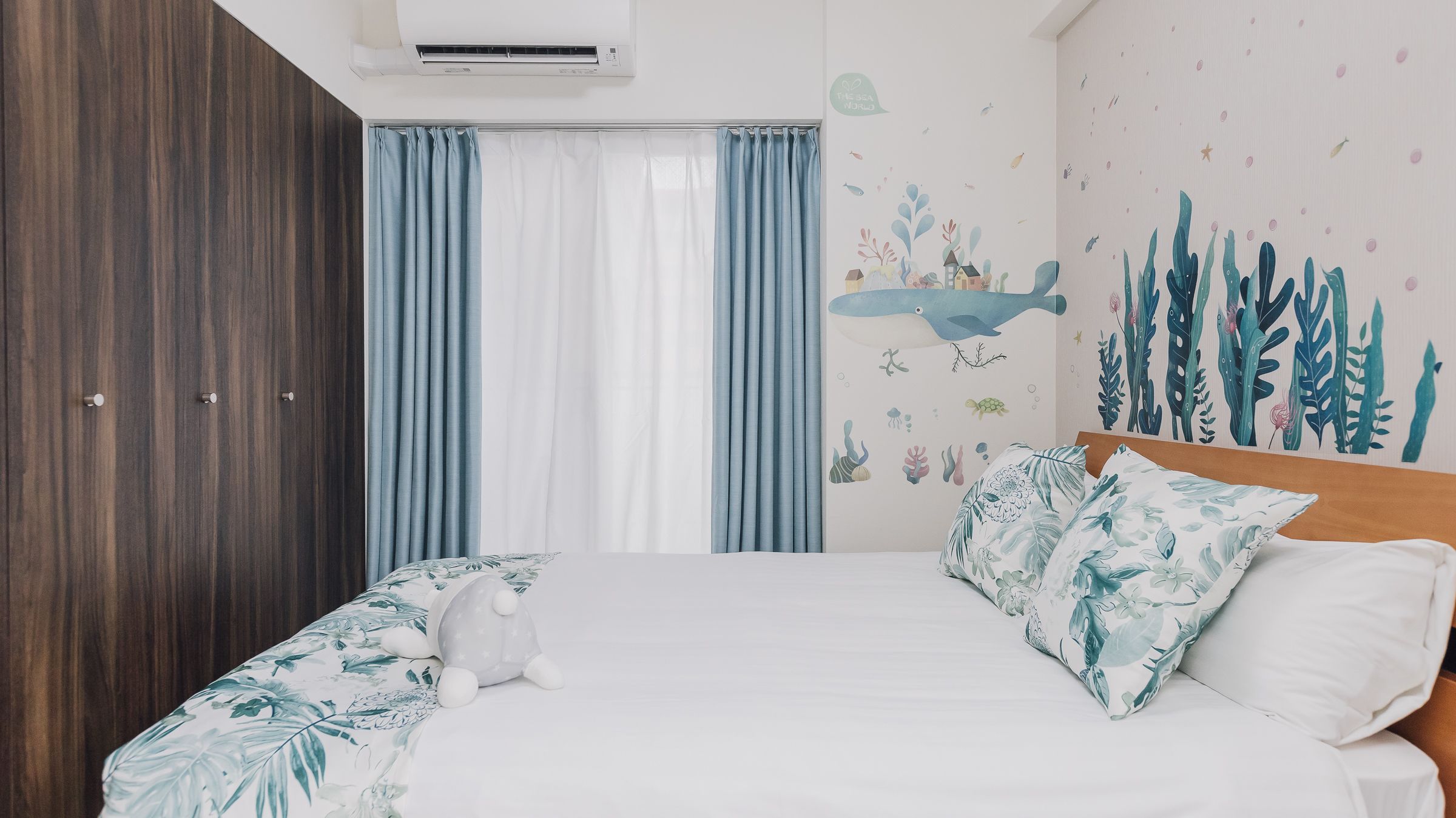A bedroom with a bed, curtains, a wall mural, and a plush toy.