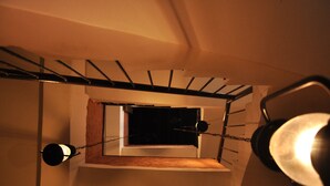 Un escalier avec une petite fenêtre en haut, un luminaire fixé au mur et un autre fixé au plafond.