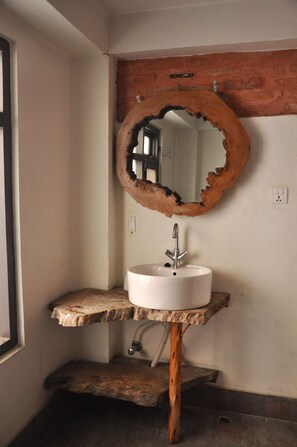 Un baño con un tocador de madera rústica, un lavabo blanco y un espejo con acabado natural y texturizado.