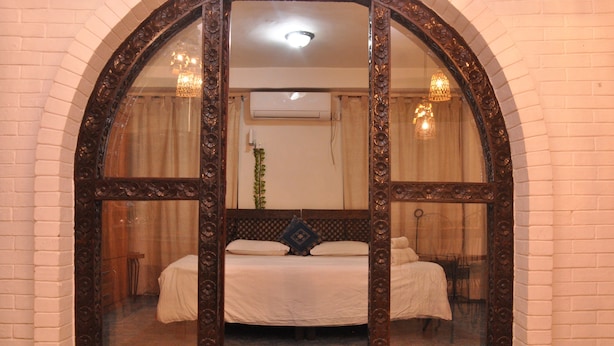 Une chambre à coucher avec un grand miroir en arc de cercle, un lit recouvert de draps blancs et un lustre.