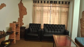 Un salon avec deux canapés en cuir noir, une table basse en verre et un mur décoratif en briques.