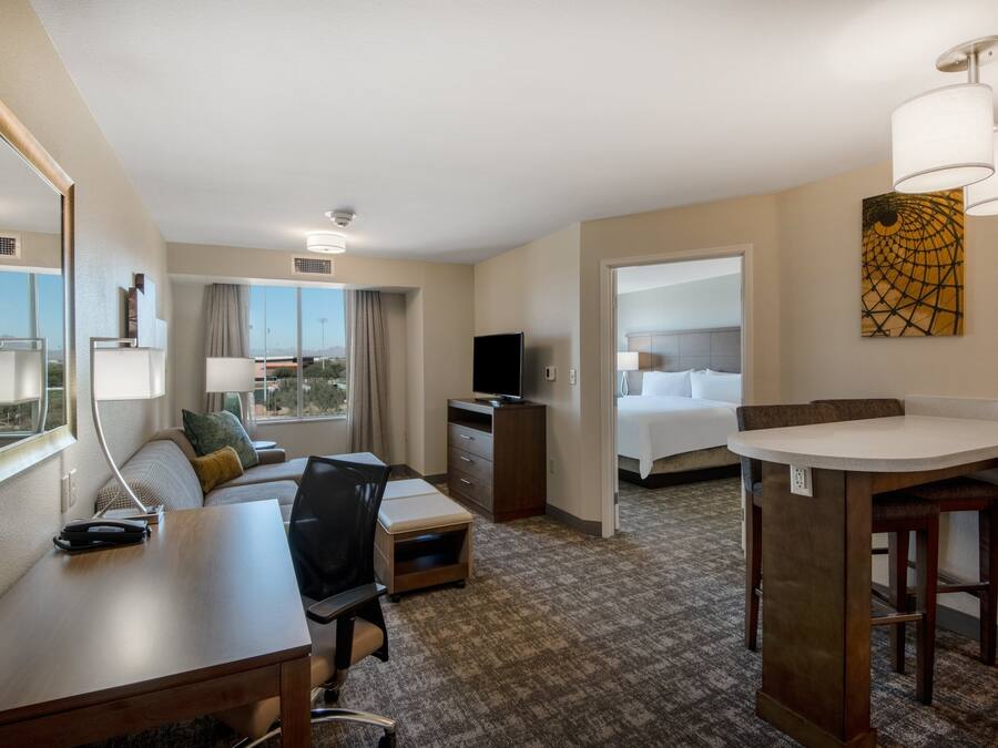 A hotel room with a desk, a bed, a TV, a sofa, a small table, and a view of the outdoors.