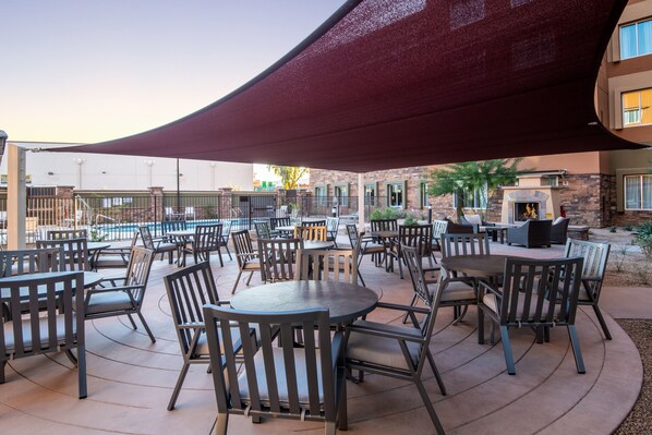 An outdoor patio area with round tables and chairs, a pool in the background, and a covered seating area. - Staybridge Suites Scottsdale - Talking Stick by IHG (Scottsdale)