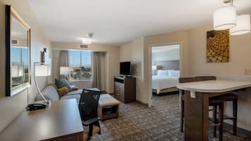 A hotel room with a desk, chair, sofa, TV, and a bed.