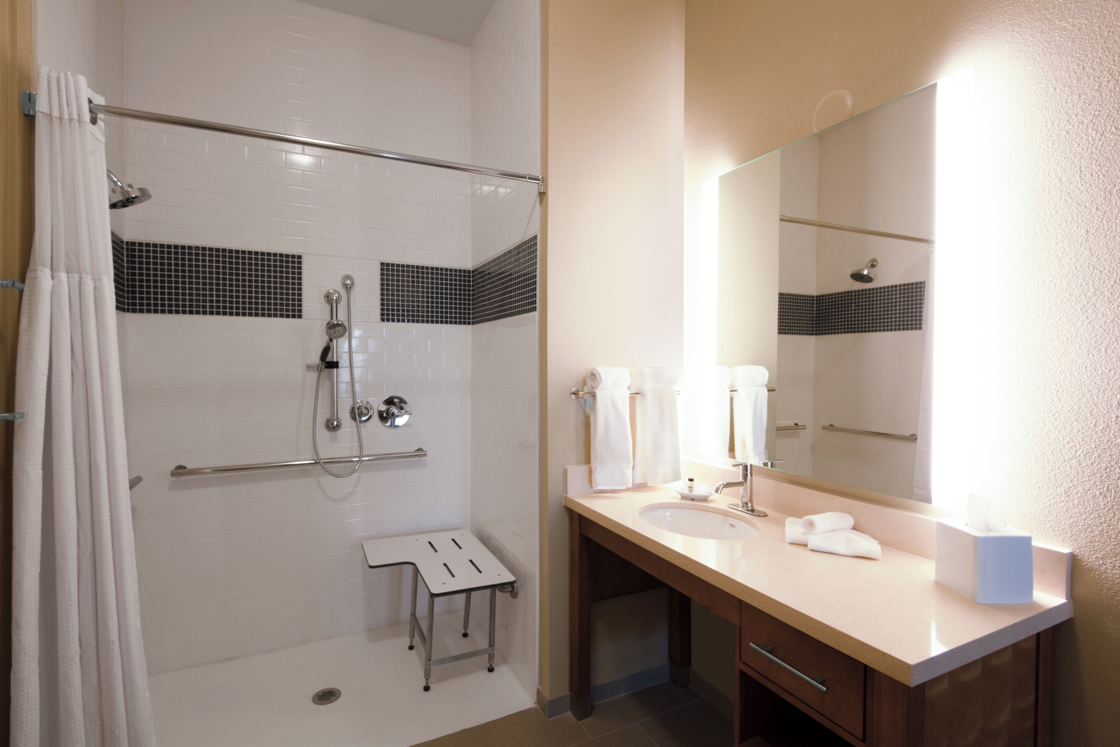 A hotel bathroom with a walk-in shower, a sink, a mirror, and a towel rack.