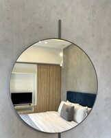 A circular mirror reflecting a modern bedroom with a bed, pillows, and a TV on a stand.