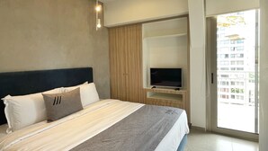 Habitación de hotel moderna con una cama grande, un televisor de pantalla plana y un ventanal corredizo al balcón.