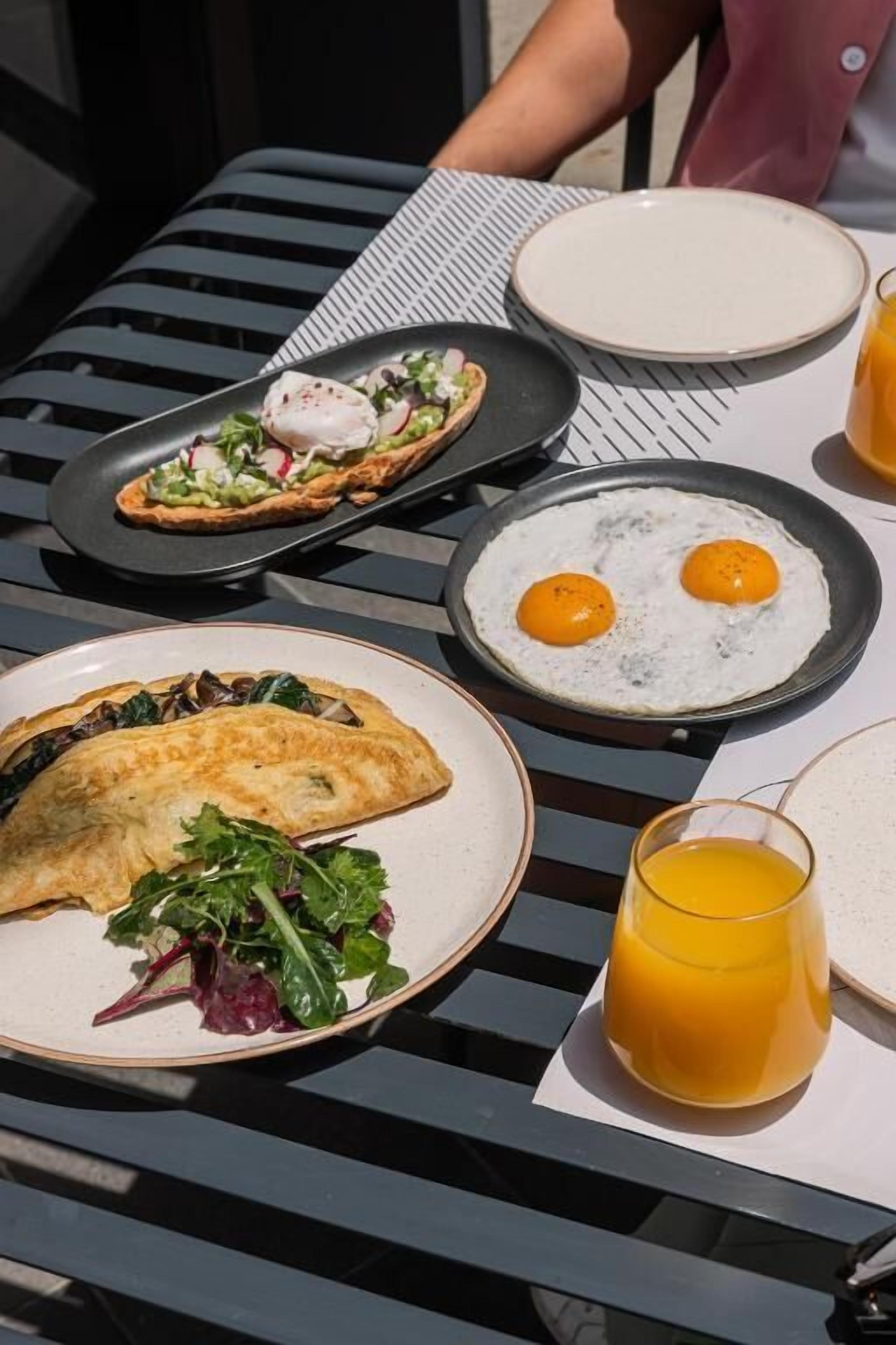 Uma mesa com itens de café da manhã, incluindo ovos, um pastel e um copo de suco de laranja.