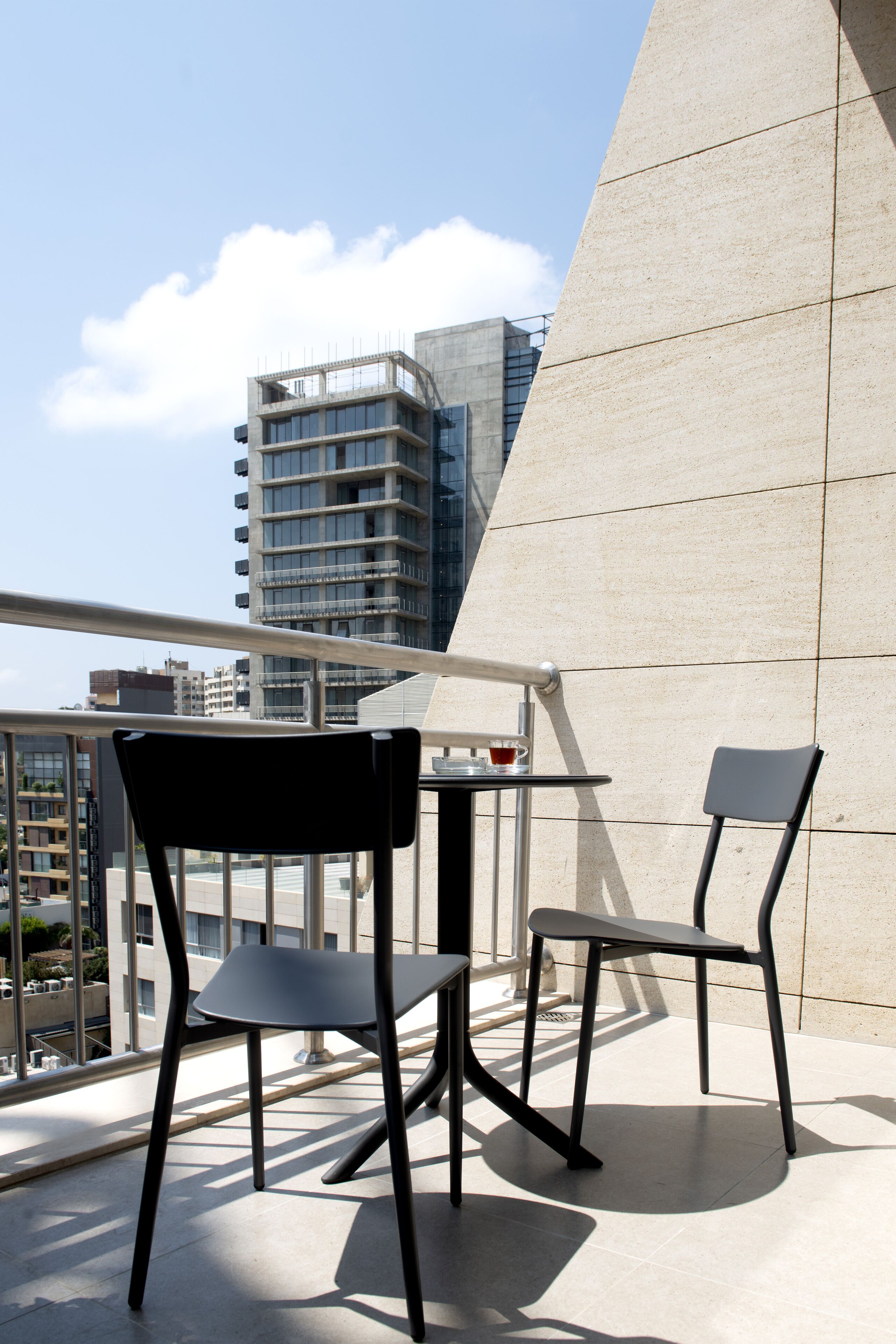 A balcony with two chairs and a small table, overlooking a cityscape with modern buildings.